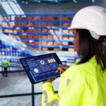 A female worker in a warehouse reviewing inventory KPI data on a tablet