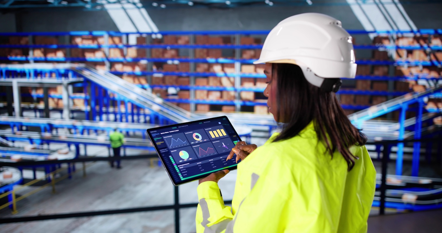 A female worker in a warehouse reviewing inventory KPI data on a tablet